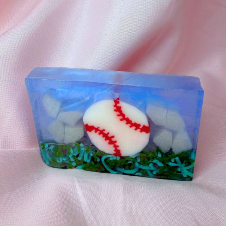 A bar of Primal Elements glycerin soap. The design is a baseball, white with red stitching, resting on some grass. The rest of the bar is blue and shite, like sky and clouds.