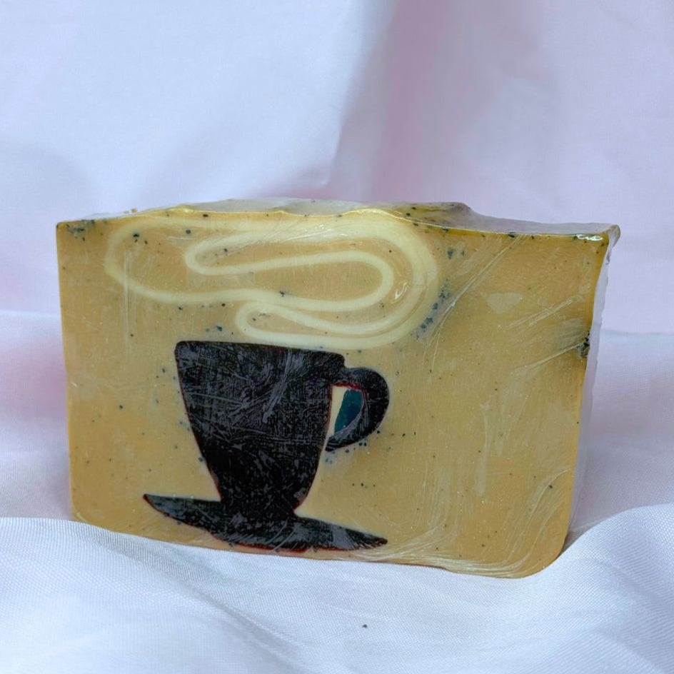 A bar of Primal Elements soap with a design of a steaming mug of coffee. Various shades of brown and visible coffee grounds.