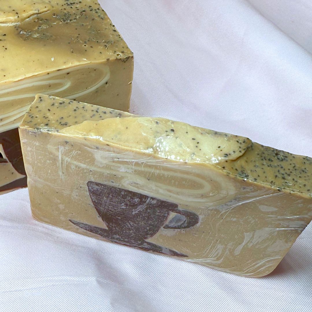 A bar of Primal Elements soap with a design of a steaming mug of coffee. Various shades of brown and visible coffee grounds. Picture taken from a high angle to show off the grounds.