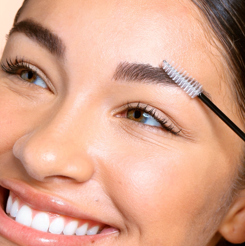 Woman applying the castor oil to her eyebrows with the spoolie applicator.