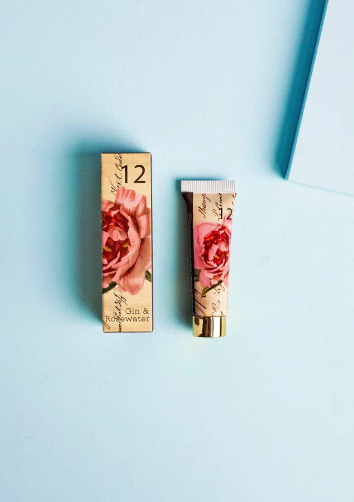 A cosmetic tube and its matching rectangular box with a pink rose print and gold lettering, placed on a light blue background.
