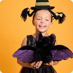 Child in a Halloween costume holding a black bat plush against an orange background. Bat is a heating pad and lavender scented