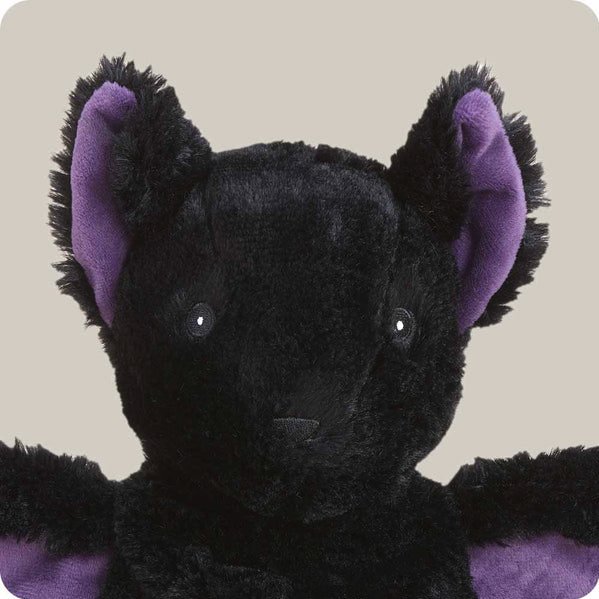 Black bat stuffed animal with purple ears and accents on a beige background