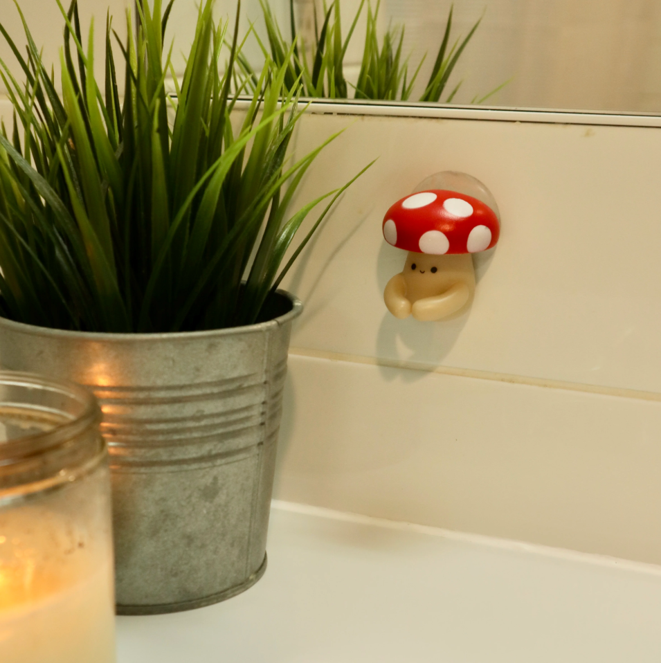 Mushroom toothbrush holder with suction cup on a wall next to a potted plant and candle