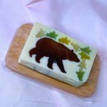 Bar of vegetable glycerin soap with a bear and tree design on a white background woodsy outdoors hiking camping summer on wooden soap dish