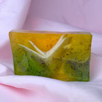 Bar of lemongrass cranberry soap with green and yellow gradient, black cranberry seeds, and white frills on a white fabric background