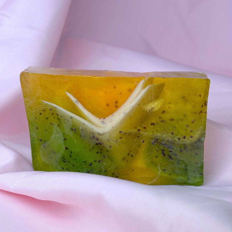 Bar of lemongrass cranberry soap with green and yellow gradient, black cranberry seeds, and white frills on a white fabric background