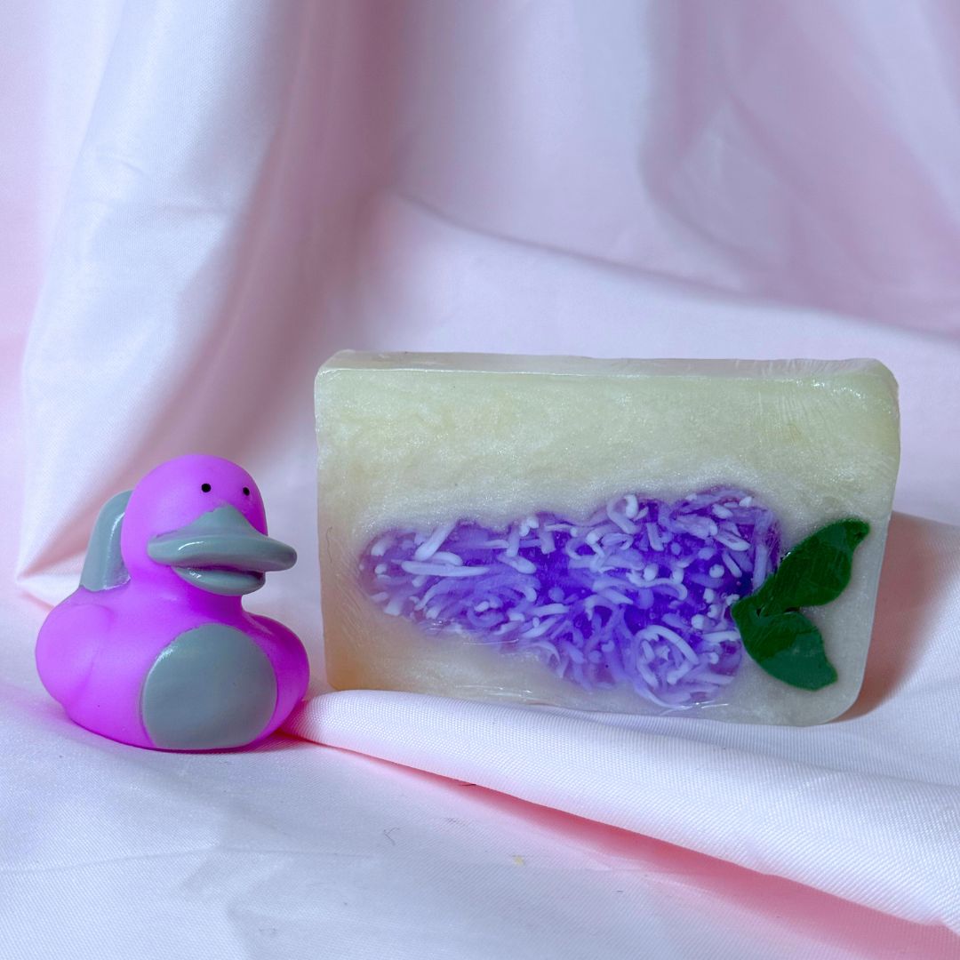 Bright purple lilac bar soap body wash soap and purple platypus duck cute gift set on pink fabric backdrop