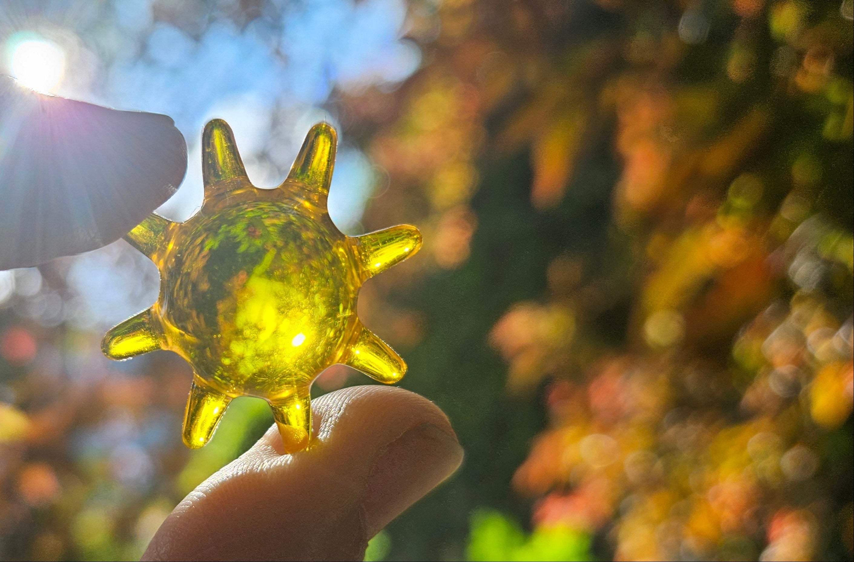 Hand holding a yellow sun shaped bath oil bead with a blurred natural background