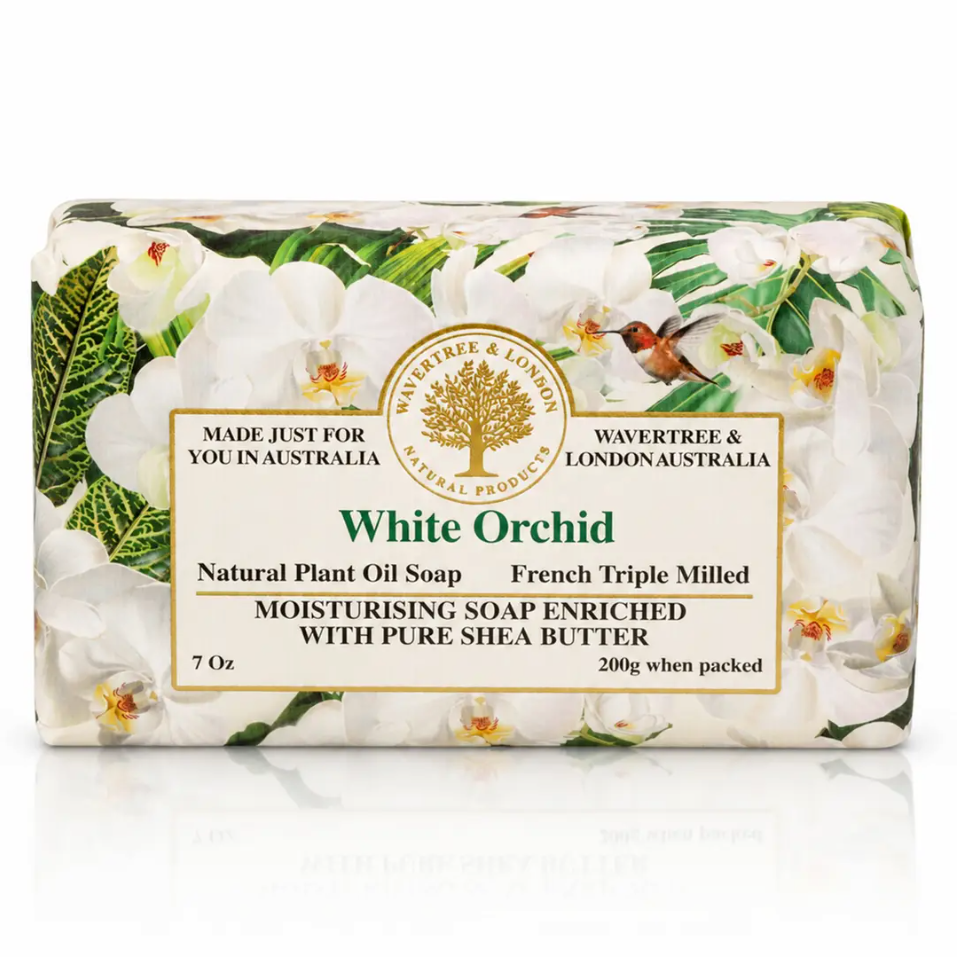 A 7 oz bar of Wavertree & London White Orchid moisturising soap, wrapped in a paper sleeve decorated with white orchid flowers and green leaves, on a white background with a soft reflection.