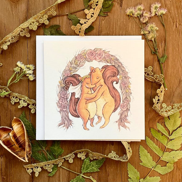 aubree sue art greeting card with watercolor illustration of squirrels getting married under a rose arch. great for wedding or anniversary. comes blank inside with envelope.