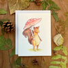aubree sue art greeting card with watercolor illustration of squirrel holding mushroom as an umbrella on a rainy day. great for any occasion or just because. woodland cottagecore style. blank inside with envelope.